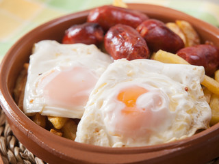 Eggs with french fries and small sausages.