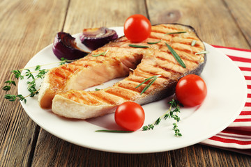 Grilled salmon and vegetables on plate on wooden background