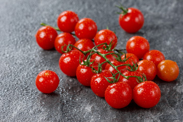 Cherry tomatoes on vine in water drops on a stone black table