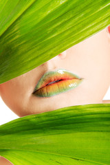 Woman with an artistic makeup behind a leaf