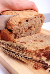 Slicing fresh bread, ears of wheat and raisins