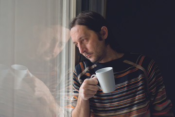 Sad man by the window drinking coffee