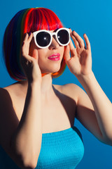 beautiful woman wearing colorful wig and white sunglasses agains
