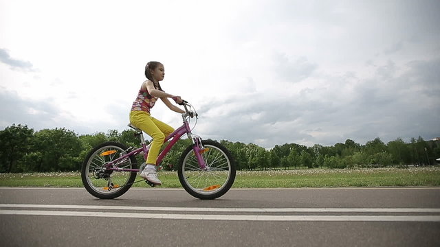 Little girl cycling in park on a pink bike in slow motion