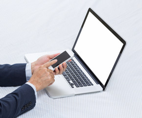 Laptop computer on bed with businessman hands holding mobile pho