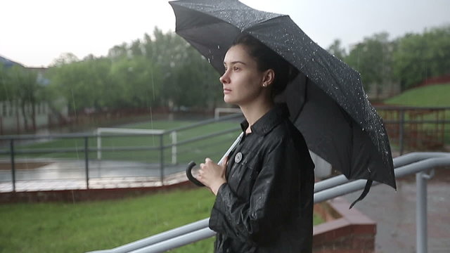 Lonely sad woman in heavy rain under an umbrella slow motion