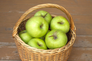 Ripe green apples in wicker basket on timber background