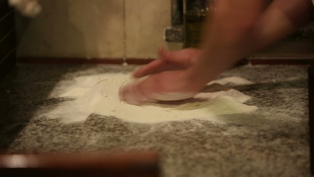 Baker hands kneading dough in flour on table