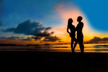 Fototapeta na wymiar silhouettes of young loving couple on bright sunset sky and sea