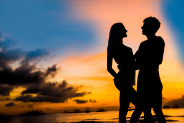 silhouettes of young loving couple on bright sunset sky and sea