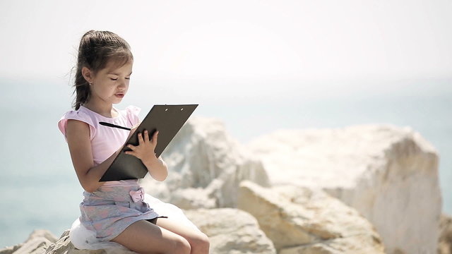 A child sits on a stone near the Adriatic Sea and draws