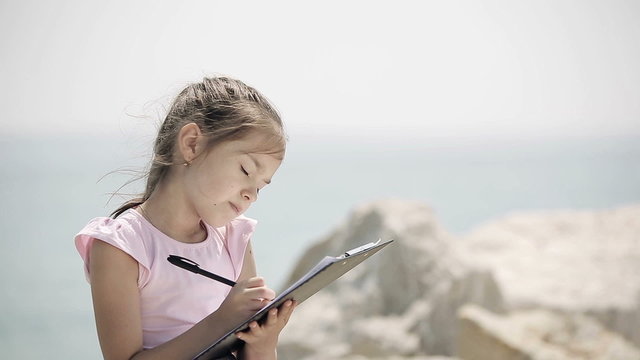 A child sits on a stone near the Adriatic Sea and draws