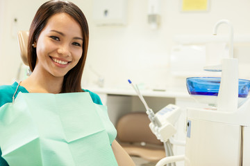 smiling asian woman sitting at the dentist and smiles towards th