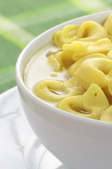 Bowl of chicken broth and tortellini on a green tablecloth.