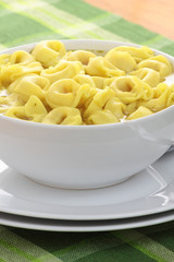 Bowl of chicken broth and tortellini on a green tablecloth.