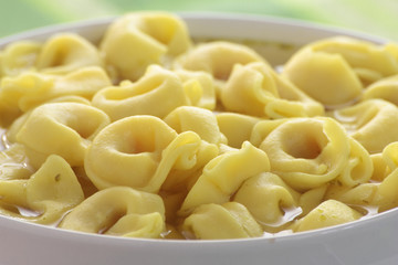 Bowl of chicken broth and tortellini on a green tablecloth.