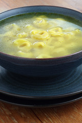 Bowl of chicken broth and tortellini on a wooden tabletop.