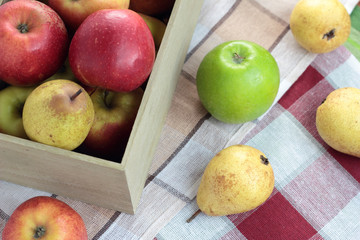 Loose apples and pears next to a box full of fruit.