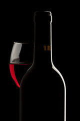 Elegant red wine bottle and wine glass in a black background