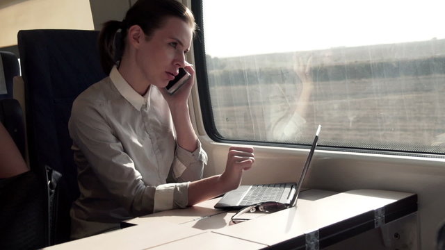 Businesswoman talking on cellphone, working on laptop on a train