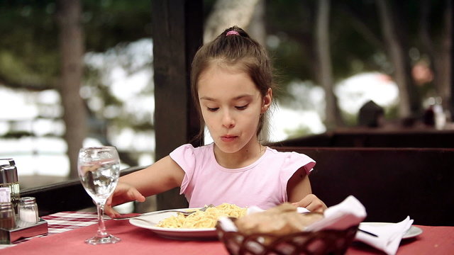 Child eats spaghetti pasta in the restaurant near the sea