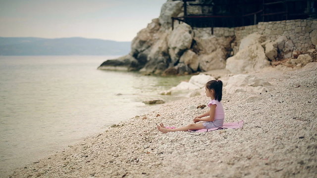 Child sits on the beach and throwing stones into the water.