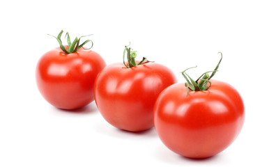 three fresh tomatoes with green leaves.