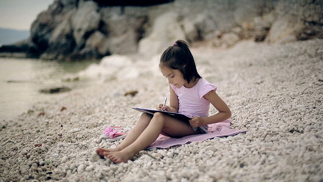 A child sits on a beach near the Adriatic Sea and draws