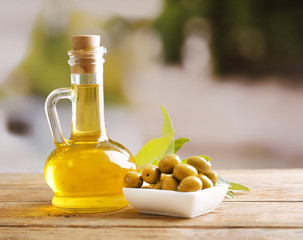 Green olives in bowl with leaves on table on light background