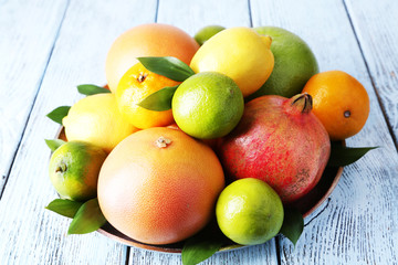 Ripe citrus with green leaves on plate on wooden background