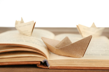 Origami boats on old book on wooden table, on white background