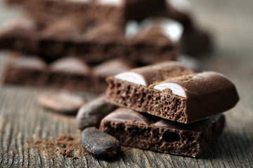 Tasty porous chocolate with cocoa beans, on wooden table
