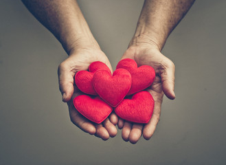 old hands of the elderly giving a red heart