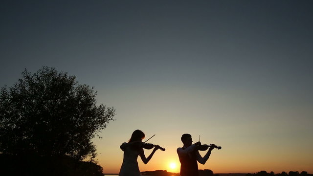Violin duet man and woman play violin on nature at the sunset.