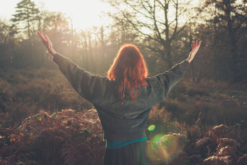 Woman raising arms joyfully at sunset in forest