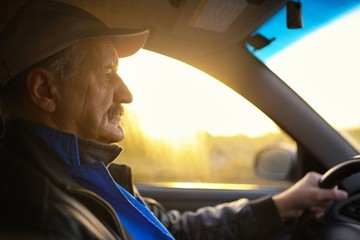 Old man with moustaches driving a car. Sun beams through a glass