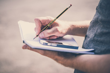 close up hands man writing on diary and smartphone