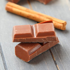 Chocolate pieces with cinnamon stick on wooden background