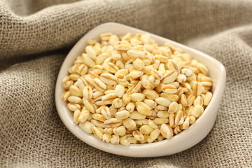 Wheat grains in white ceramic bowl on sackcloth background