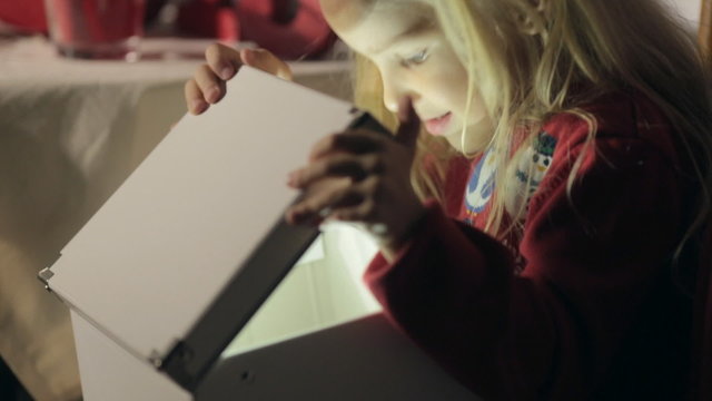 Cute little blond girl opens a Christmas gift with a miracle