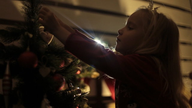 Little blond girl with long hair decorates Christmas tree with