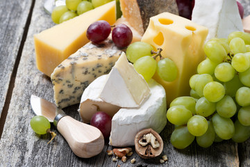 assortment of fresh cheeses and grapes on a wooden background