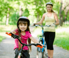 Obraz premium mom and daughter ride bikes in the forest