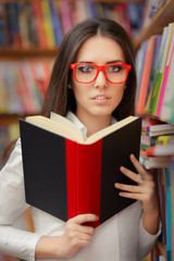 Young Woman with Glasses Reading Near Bookshelf