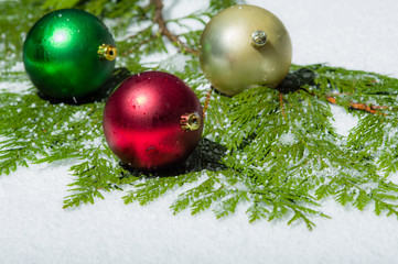 Three Christmas balls in the snow with cedar