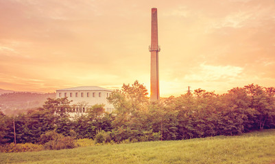 Factory building at summer sunset behind trees