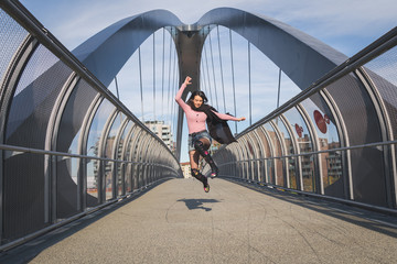 Beautiful young brunette jumping on a bridge