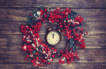 Holly christmas wreath with clock on wooden table.