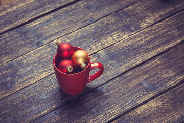 Cup with christmas balls on wooden table.