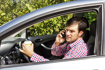 Young man speaking on phone and drinking coffee while driving